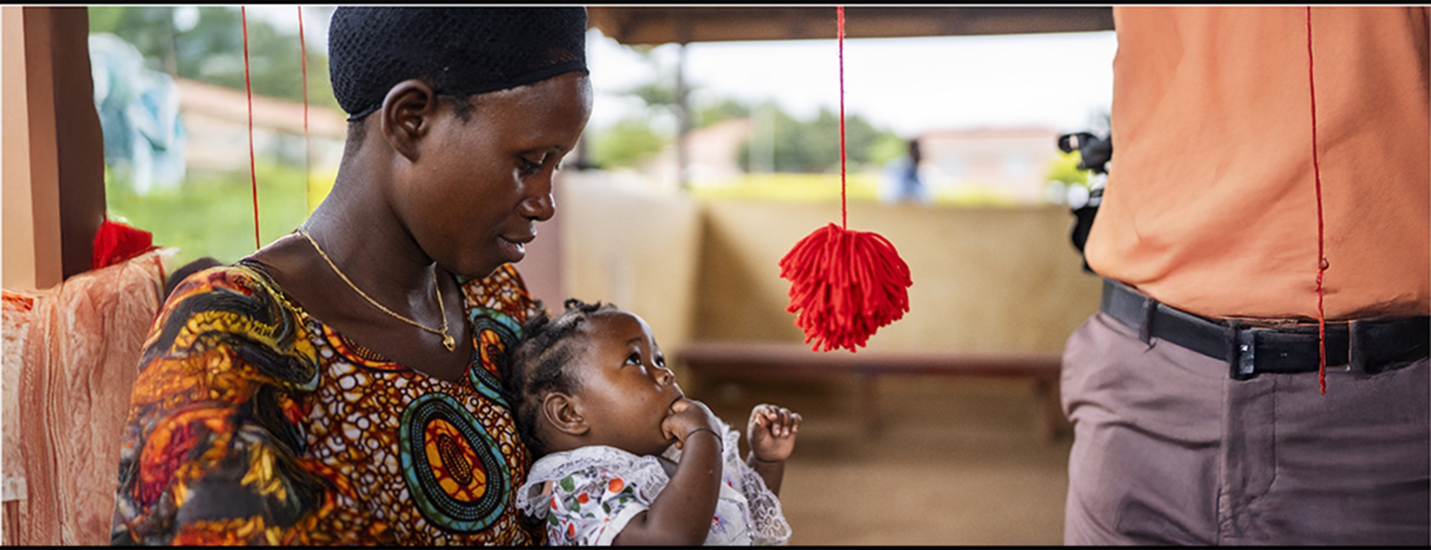 Woman holding her baby who is focused on a red hanging pom pom